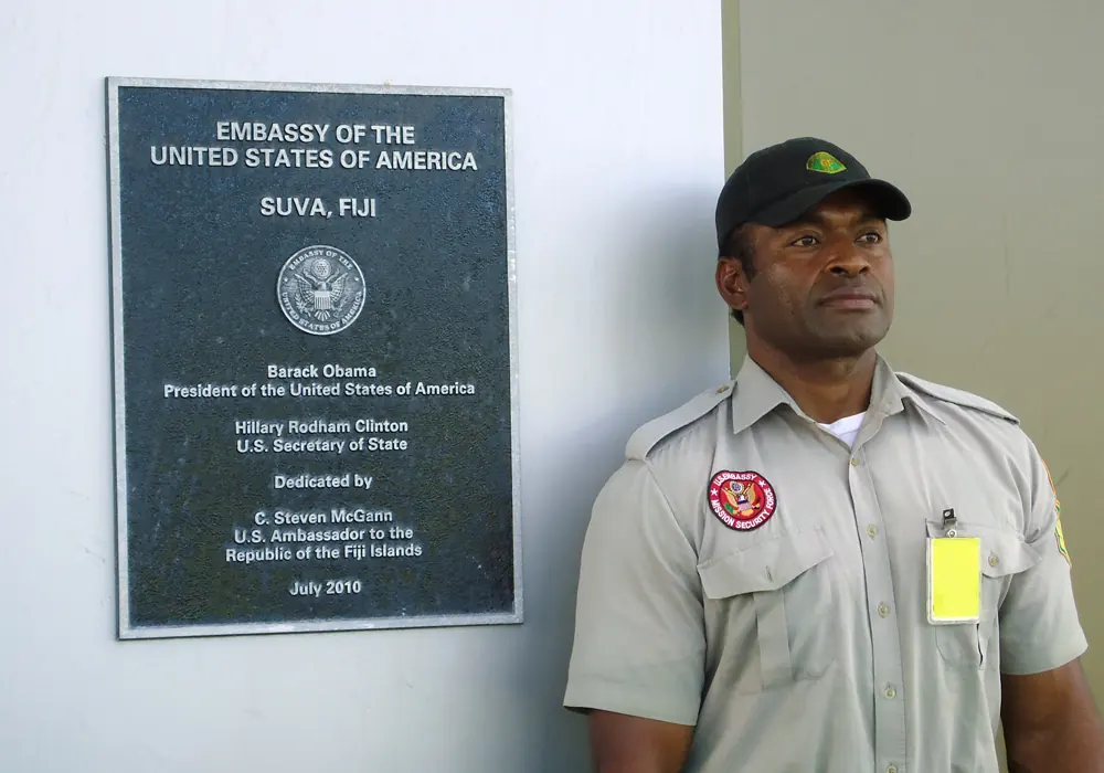 Guardforce officer beside an embassy plaque